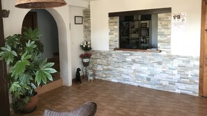 A spacious living area with a large potted plant, a wicker chair, and a hanging light fixture. - Posada La Maza (Arnuero)