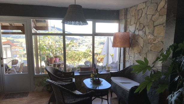 A cozy room with wicker furniture, a stone wall, and a view of greenery outside. - Posada La Maza (Arnuero)