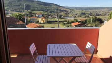 A balcony with a table and chairs, overlooking a rural landscape with houses and hills.