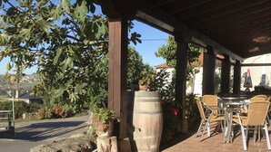 An outdoor patio area with a wooden pergola, a stone bench, and a large barrel. - Posada La Maza (Arnuero)
