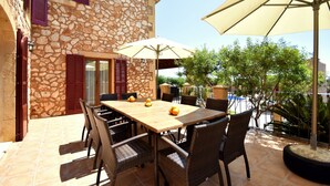 An outdoor patio with a stone building, a wooden table with chairs, and two umbrellas. - 44059 Sa Torre nova - 44059 S'Illot - Sa Torre nova (San Lorenzo)