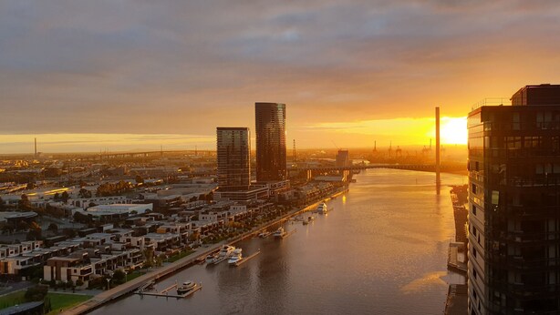 Eine Stadtansicht mit modernen Gebäuden, einem Fluss und einer Brücke bei Sonnenuntergang.