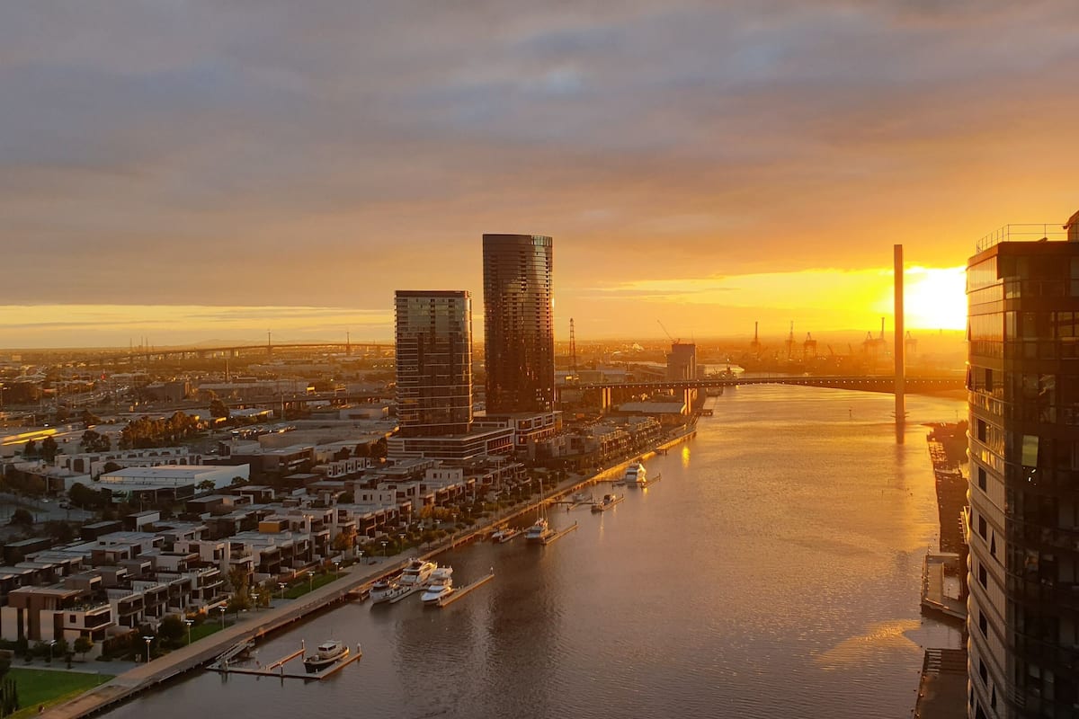 Une vue d’une ville avec des bâtiments modernes, une rivière et un pont, au coucher du soleil.
