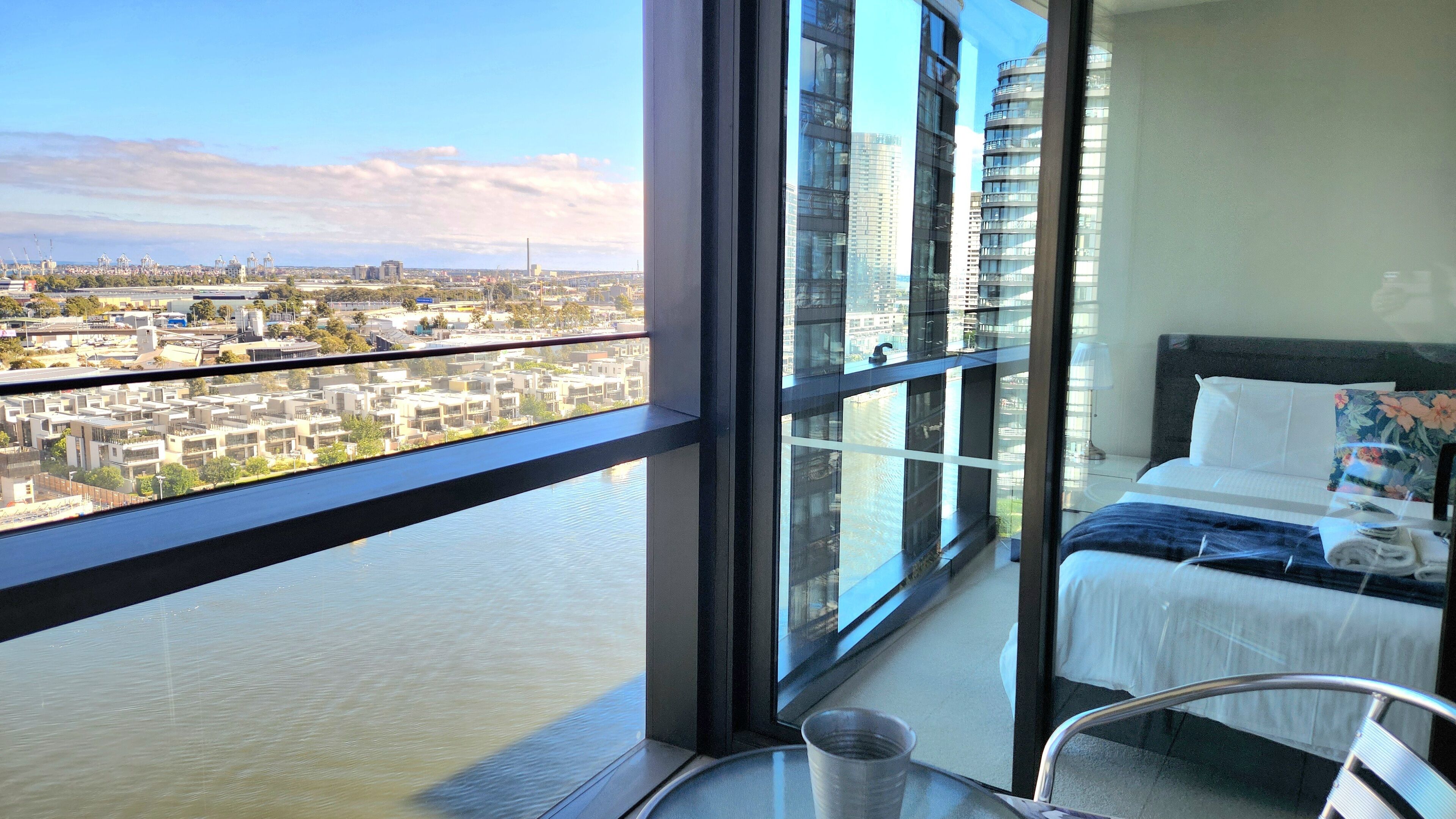 A high-rise hotel room with a large window offering a city view, a bed with white linens, and a small table with a glass top.