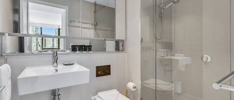 Un baño moderno con ducha de vidrio, un lavamanos blanco y un inodoro.