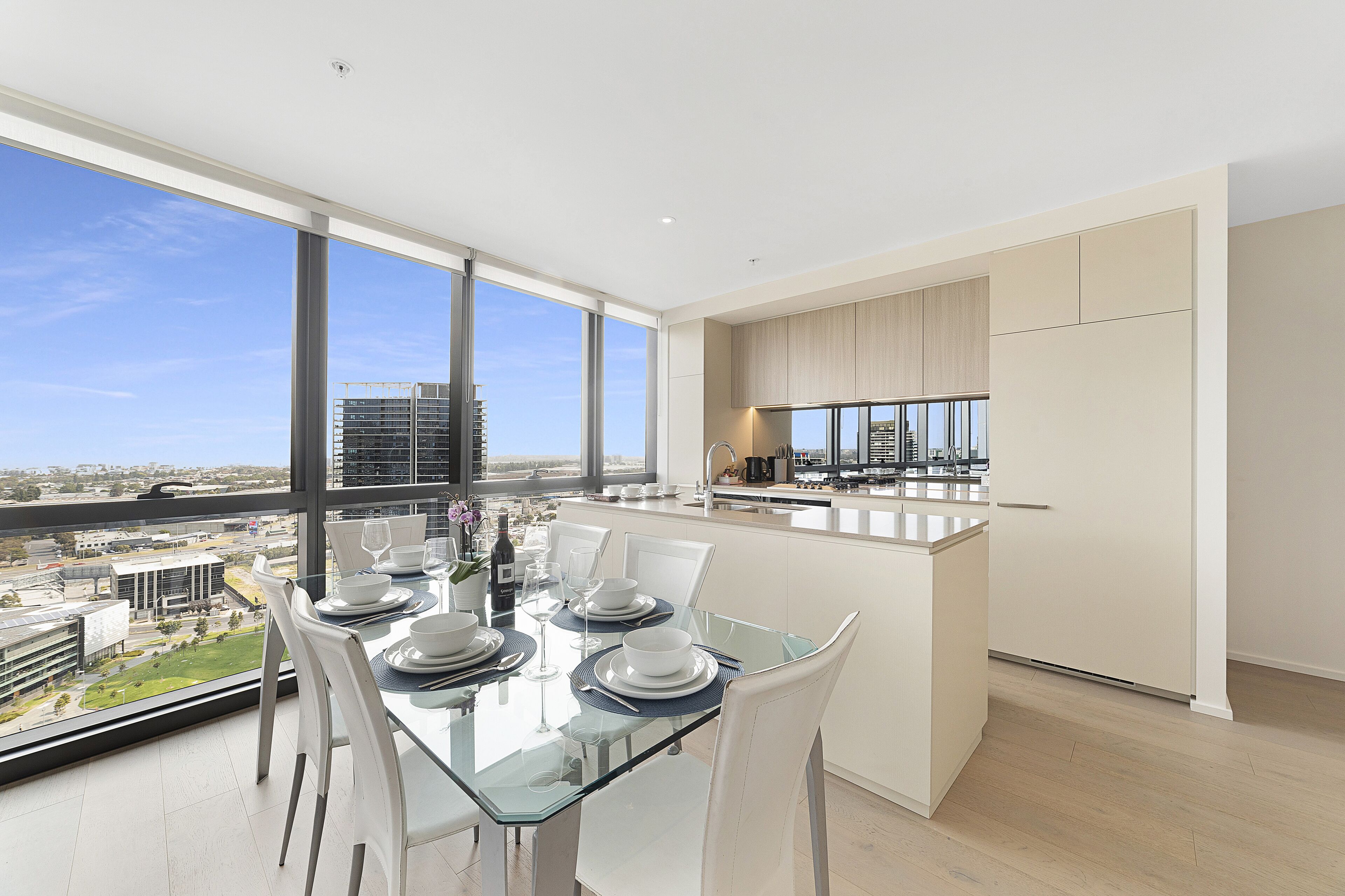 A modern kitchen with a large island, a dining area with a glass table, and a view of the cityscape.