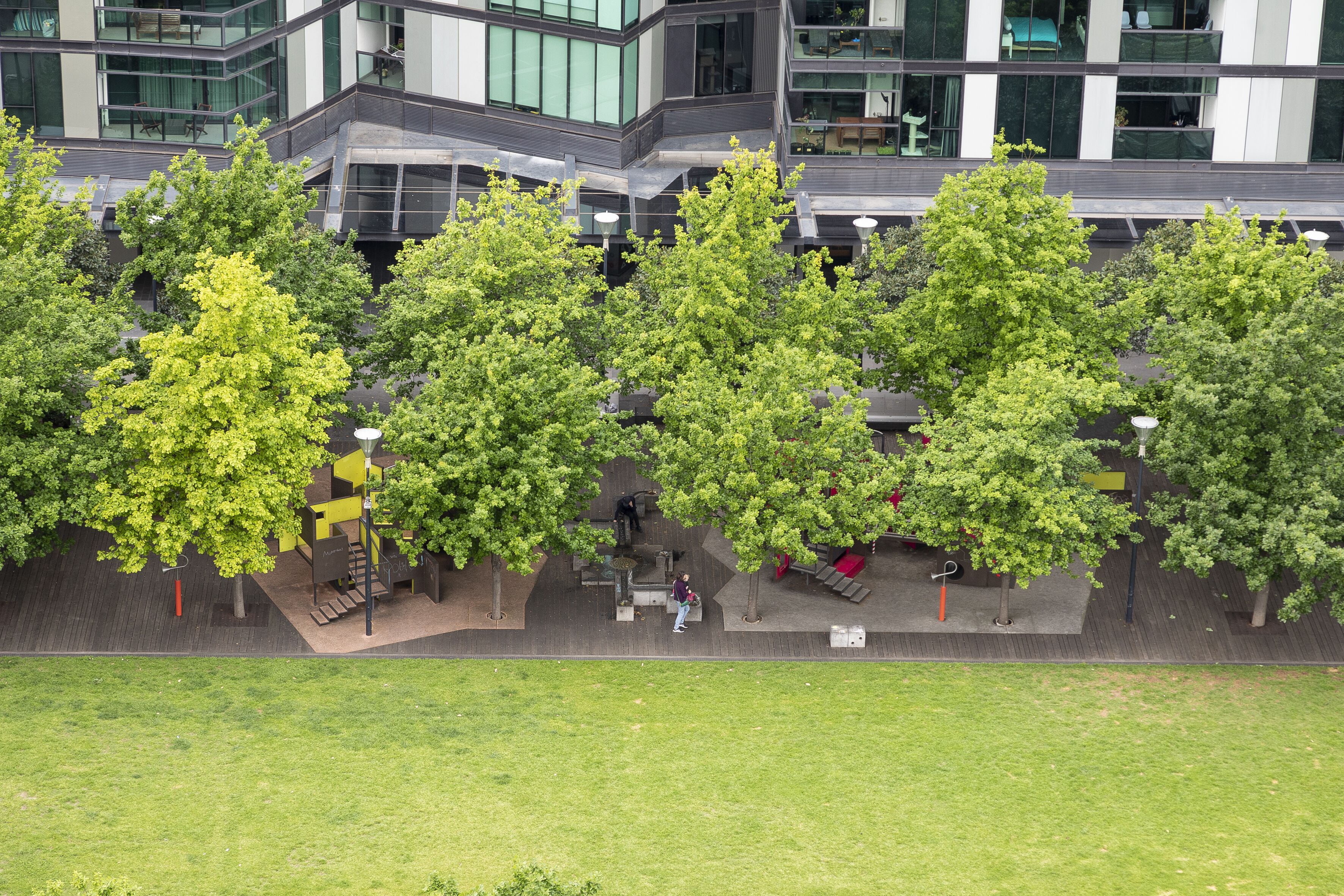 A modern building with a glass facade, outdoor seating, and trees.