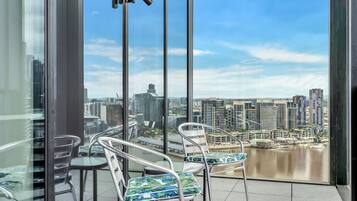 Un balcón con vista a la ciudad, sillas de metal y una mesa de vidrio.