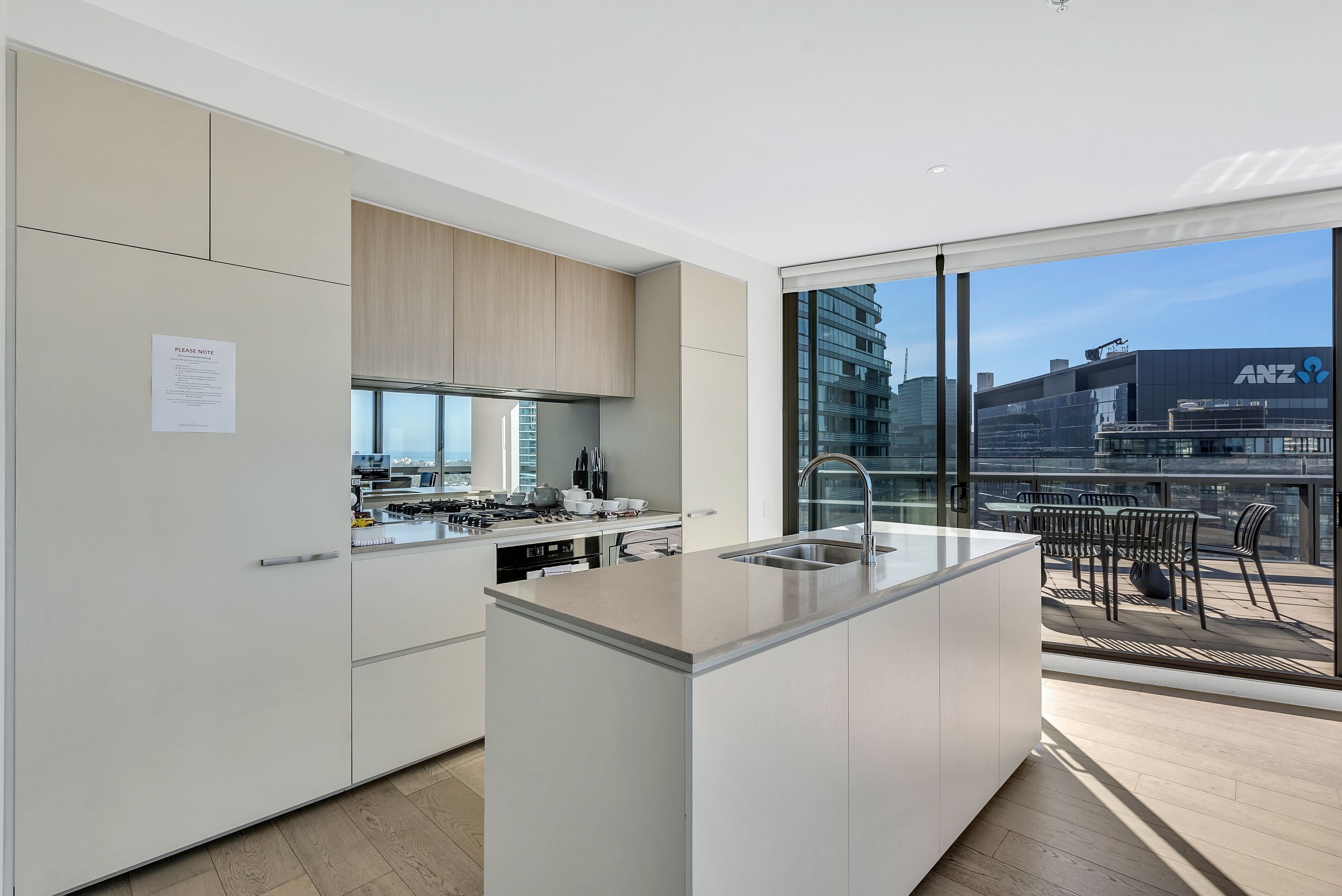 A modern kitchen with a large island, a built-in oven, and a view of a cityscape through large windows.