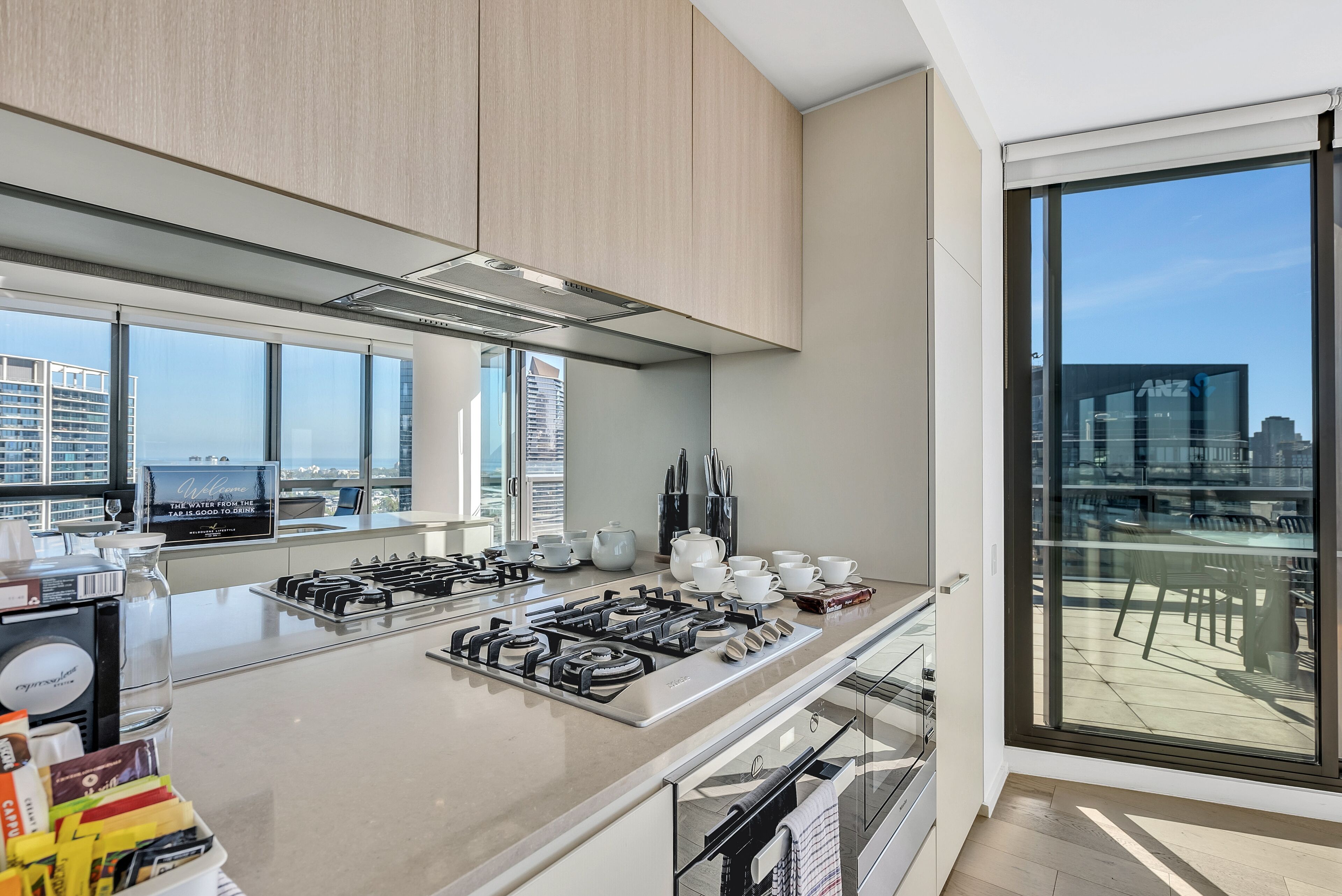 A modern kitchen with a large island, stainless steel appliances, and a city view through large windows.