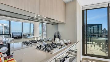 A modern kitchen with a large island, stainless steel appliances, and a city view through large windows.
