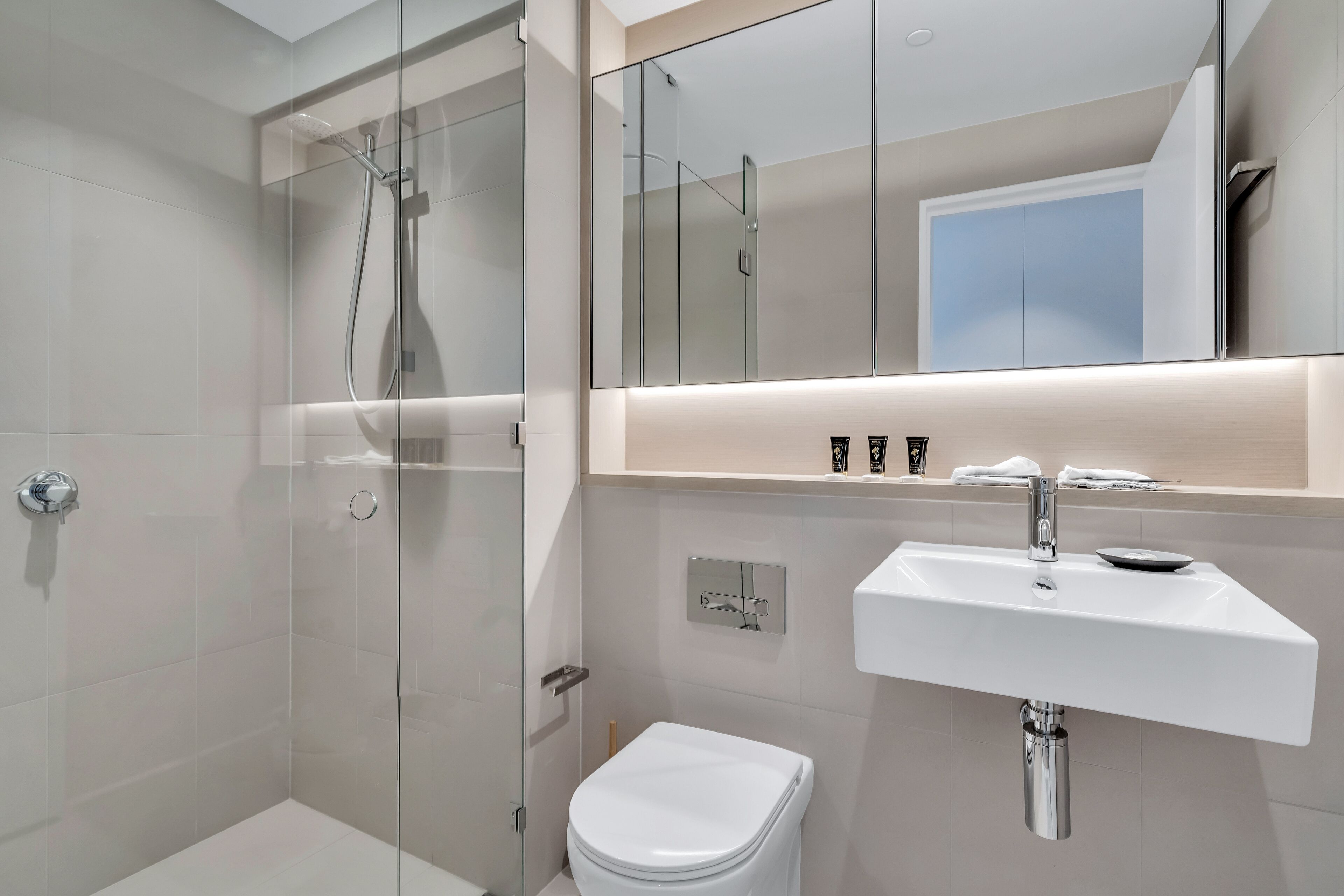 Un baño moderno con cabina de ducha de vidrio, inodoro blanco y lavabo con espejo sobre él.