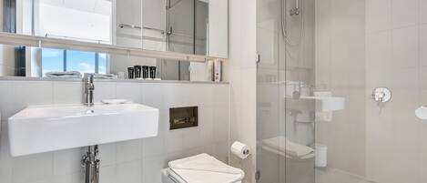 Un baño moderno con lavamanos blanco, inodoro y cabina de ducha con paredes de vidrio.