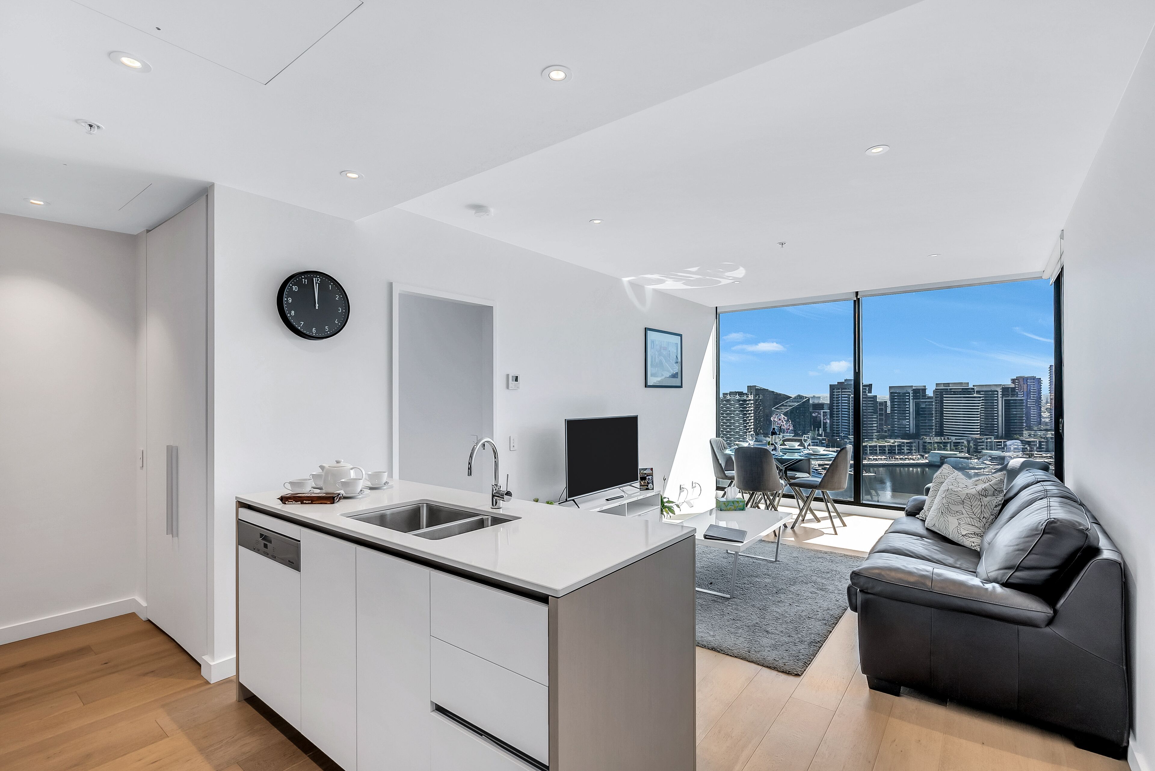 A modern kitchen with a central island, a dining area with a black sofa, and a large window with a city view.
