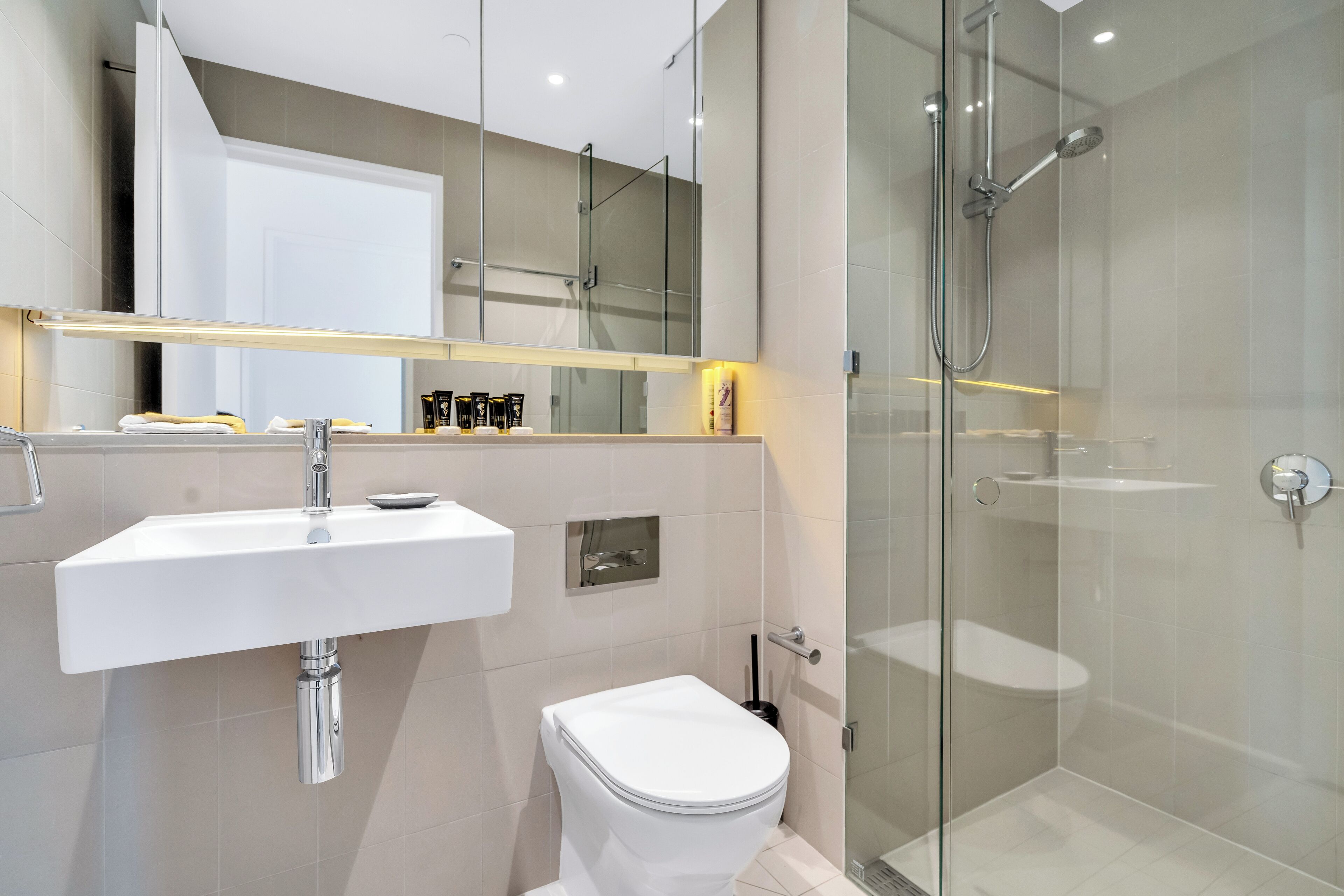 Une salle de bain moderne avec un lavabo blanc, des toilettes et une douche séparée par une paroi de verre.