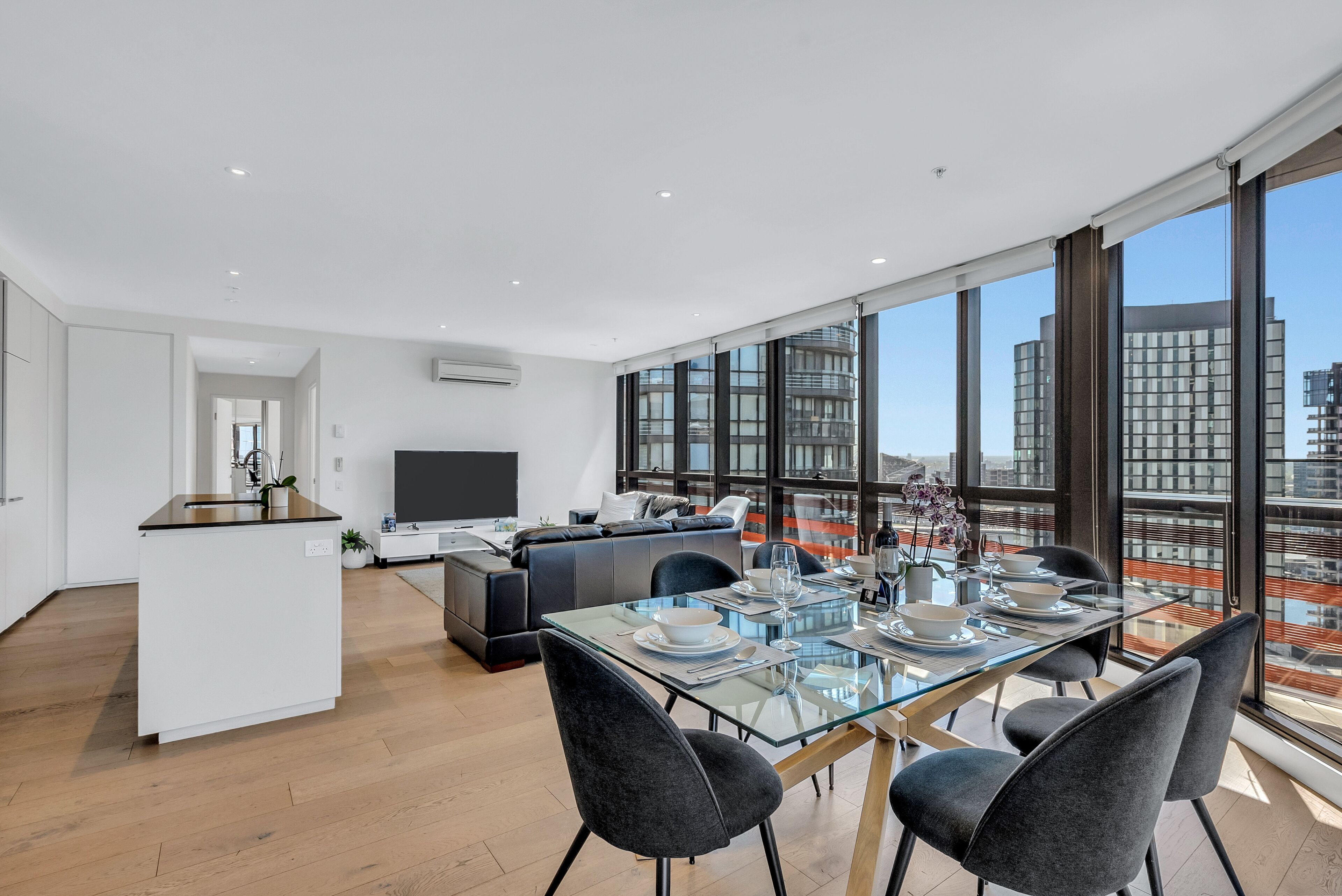 A modern apartment with a dining area, kitchen, and living space with large windows offering city views.
