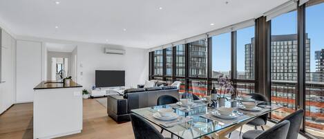 A modern apartment with a dining area, kitchen, and living space with large windows offering city views.
