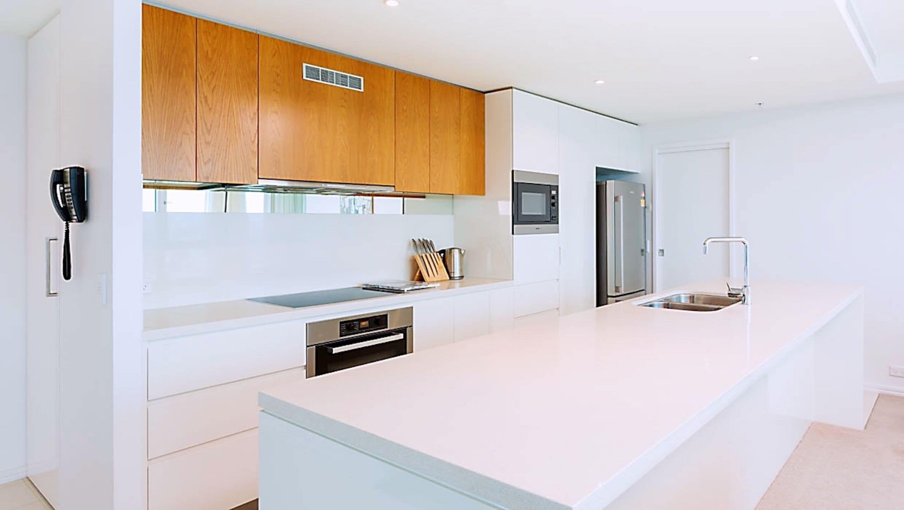 A modern kitchen with white cabinetry, a built-in oven, a stainless steel refrigerator, and a large island with a sink.