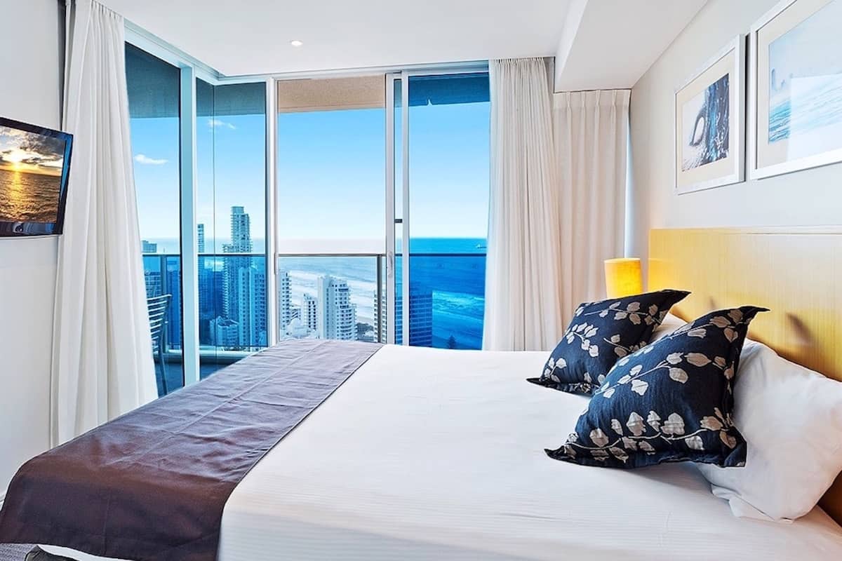 Een hotelkamer met een groot bed, een stadszicht door kamerhoge ramen en een panoramisch uitzicht vanaf het balkon.