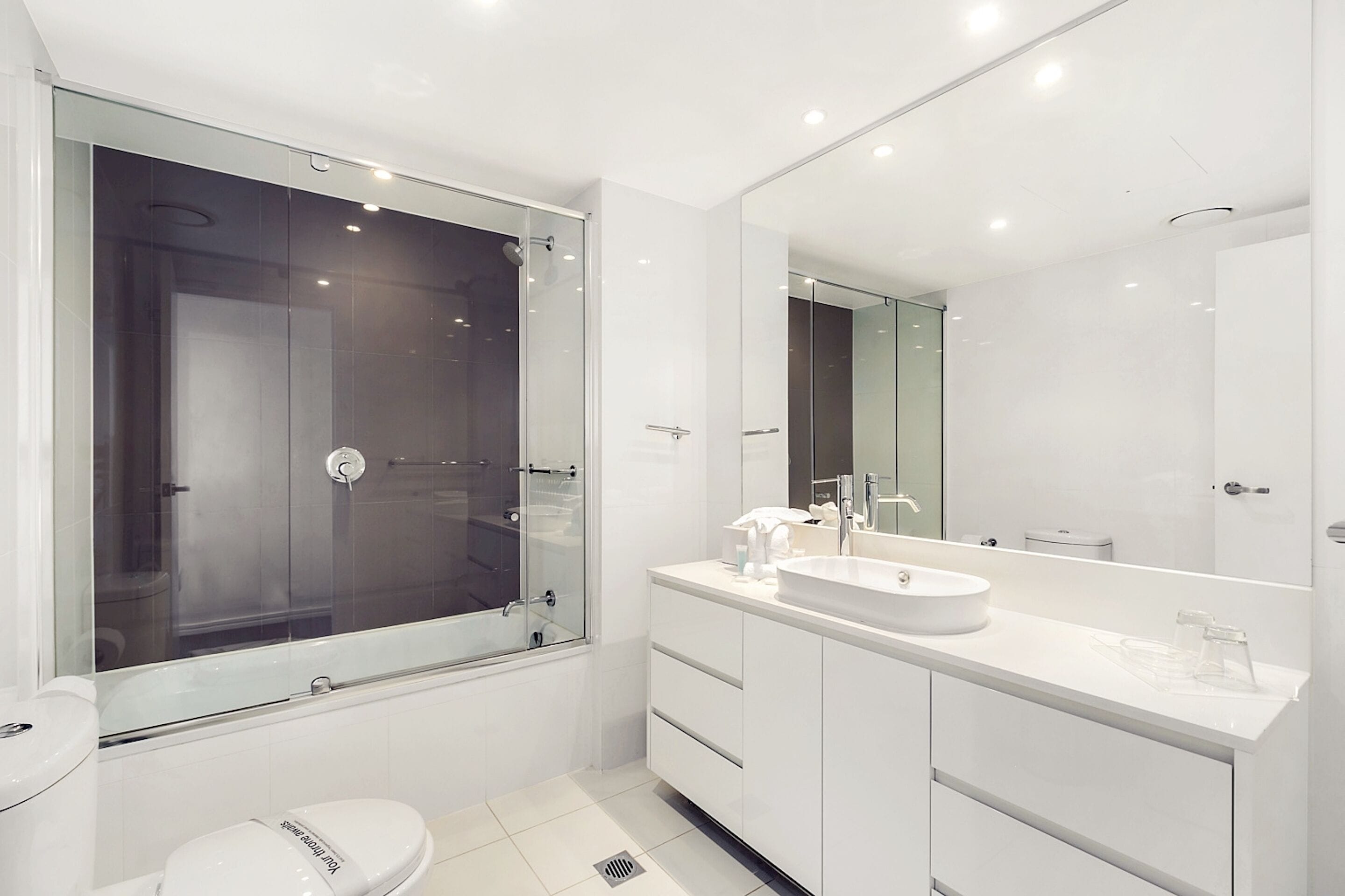 Un baño moderno con ducha de vidrio, lavamanos blanco y un espejo grande.