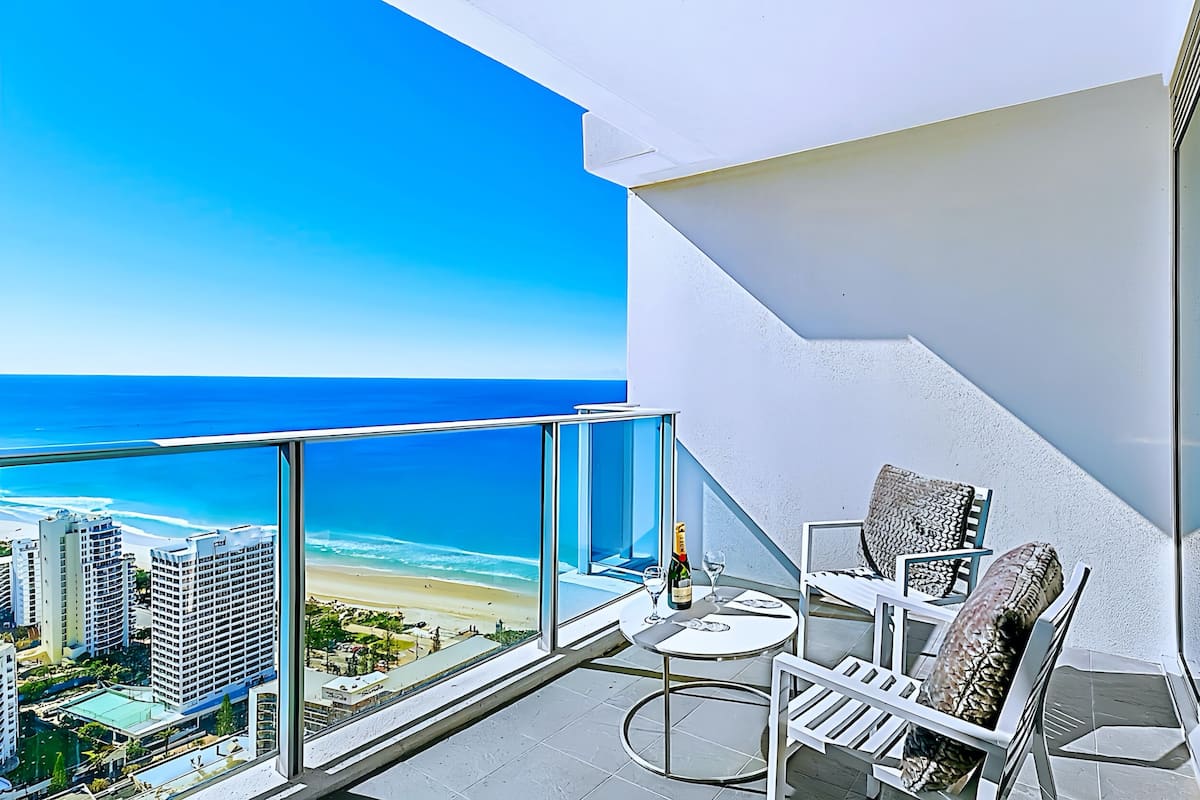 Een balkon met glazen hekwerk met uitzicht op een strand en stadsbeeld.
