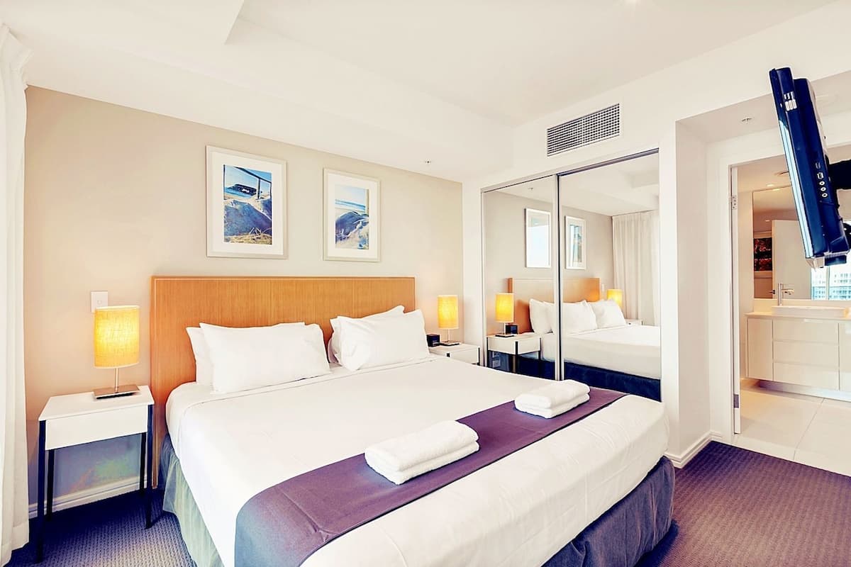 Een hotelkamer met een groot bed, twee bedlampjes, een spiegel en kunst aan de muur.