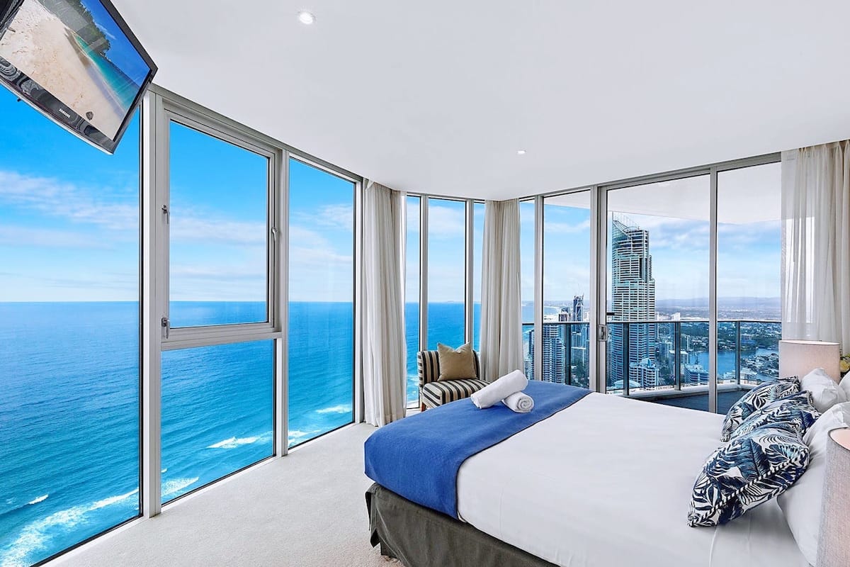 Hotelkamer in een hoog gebouw met een groot bed, uitzicht op de oceaan en een stadsgezicht.
