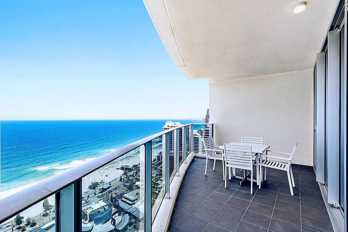 Een balkon met uitzicht op de oceaan, witte stoelen en een betegelde vloer.