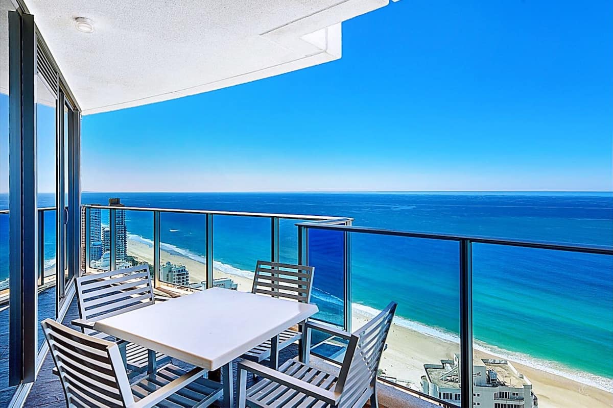 Een balkon met een tafel en stoelen met uitzicht op een strand en de oceaan.
