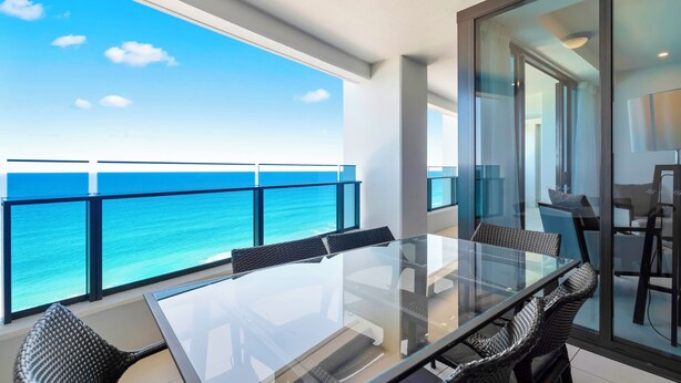 A balcony with a glass table and chairs, overlooking a turquoise sea. - H Luxury Residence Apartments - Holiday Paradise (Surfers Paradise)