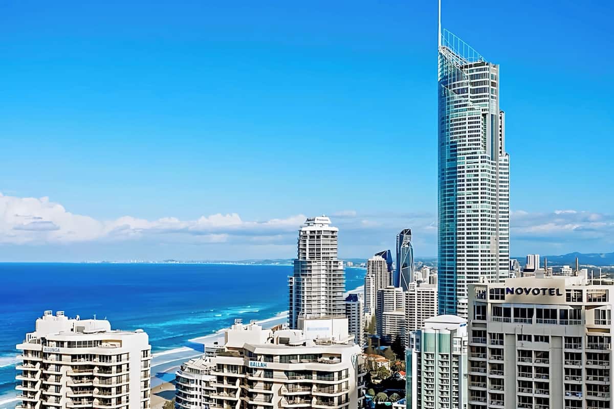 Een modern hotel met veel verdiepingen, dichtbij een strand met helderblauw water.