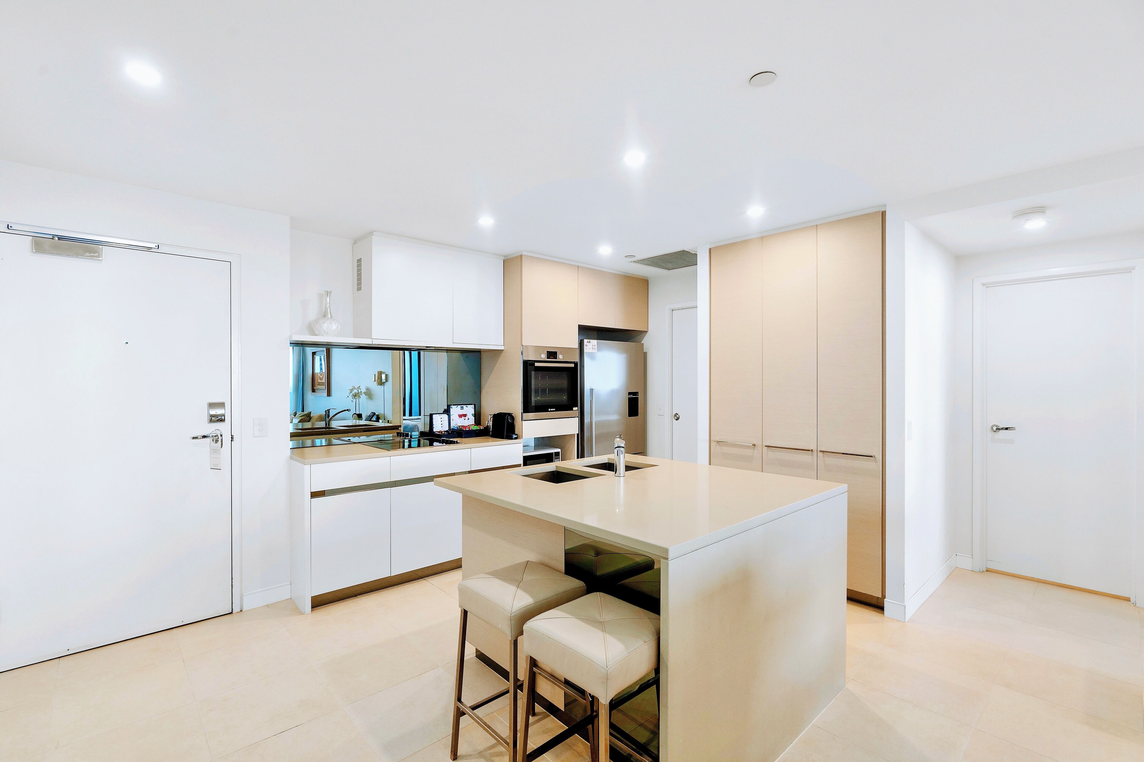 A modern kitchen with a central island, bar stools, a microwave, and a refrigerator.