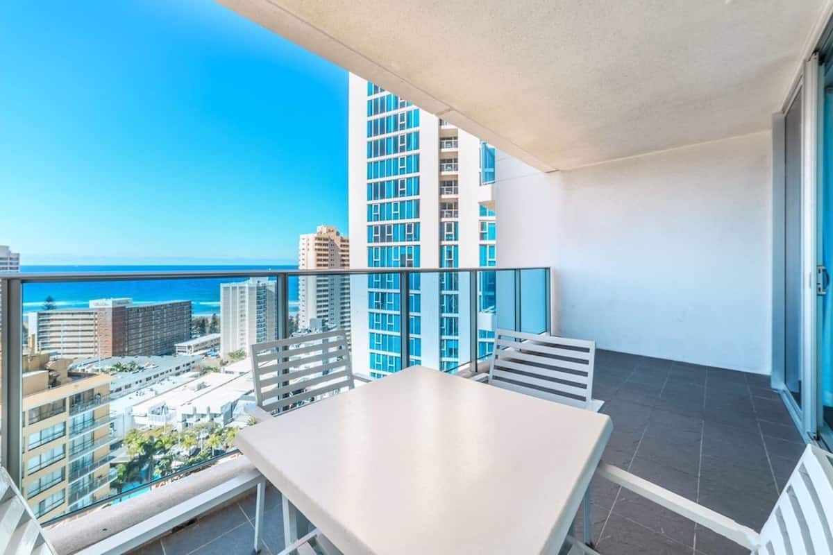 Een balkon met een tafel en stoelen, met uitzicht op een stadslandschap en de oceaan.