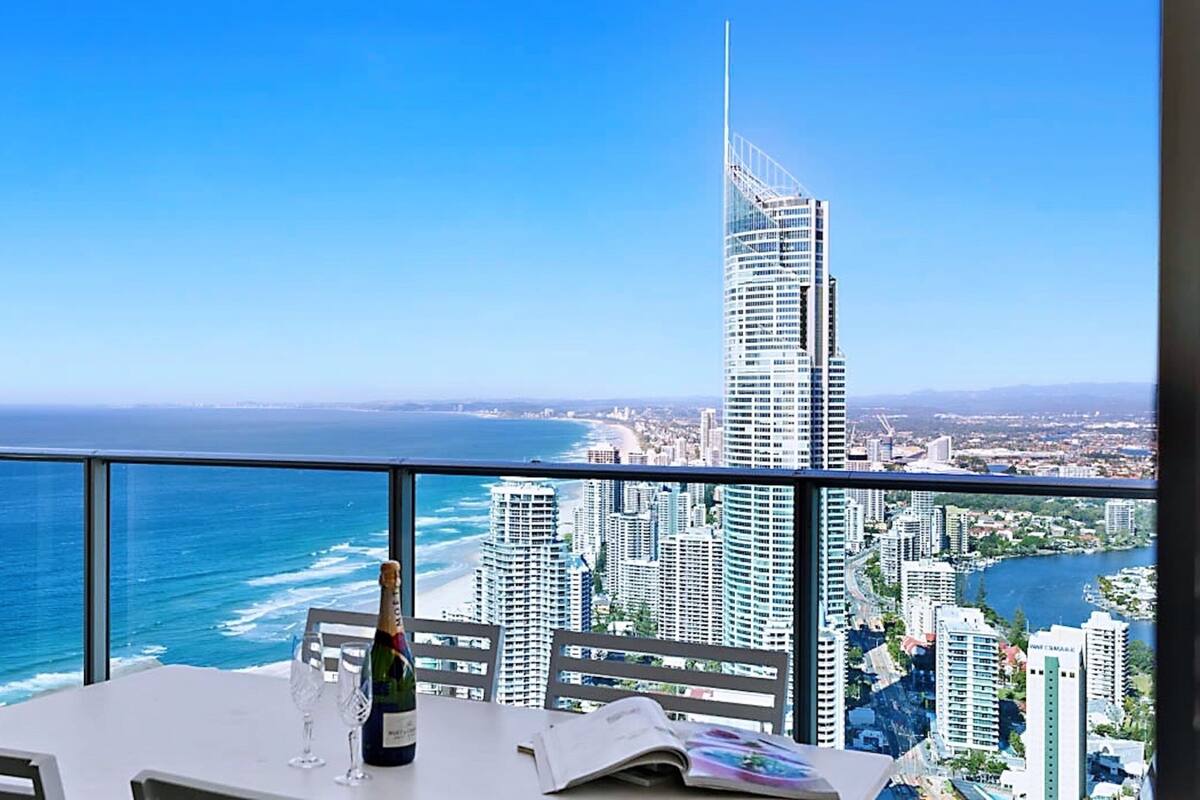 Een balkon met een tafel, een fles champagne en een menukaart. In de verte is een hoog gebouw en de kustlijn te zien.
