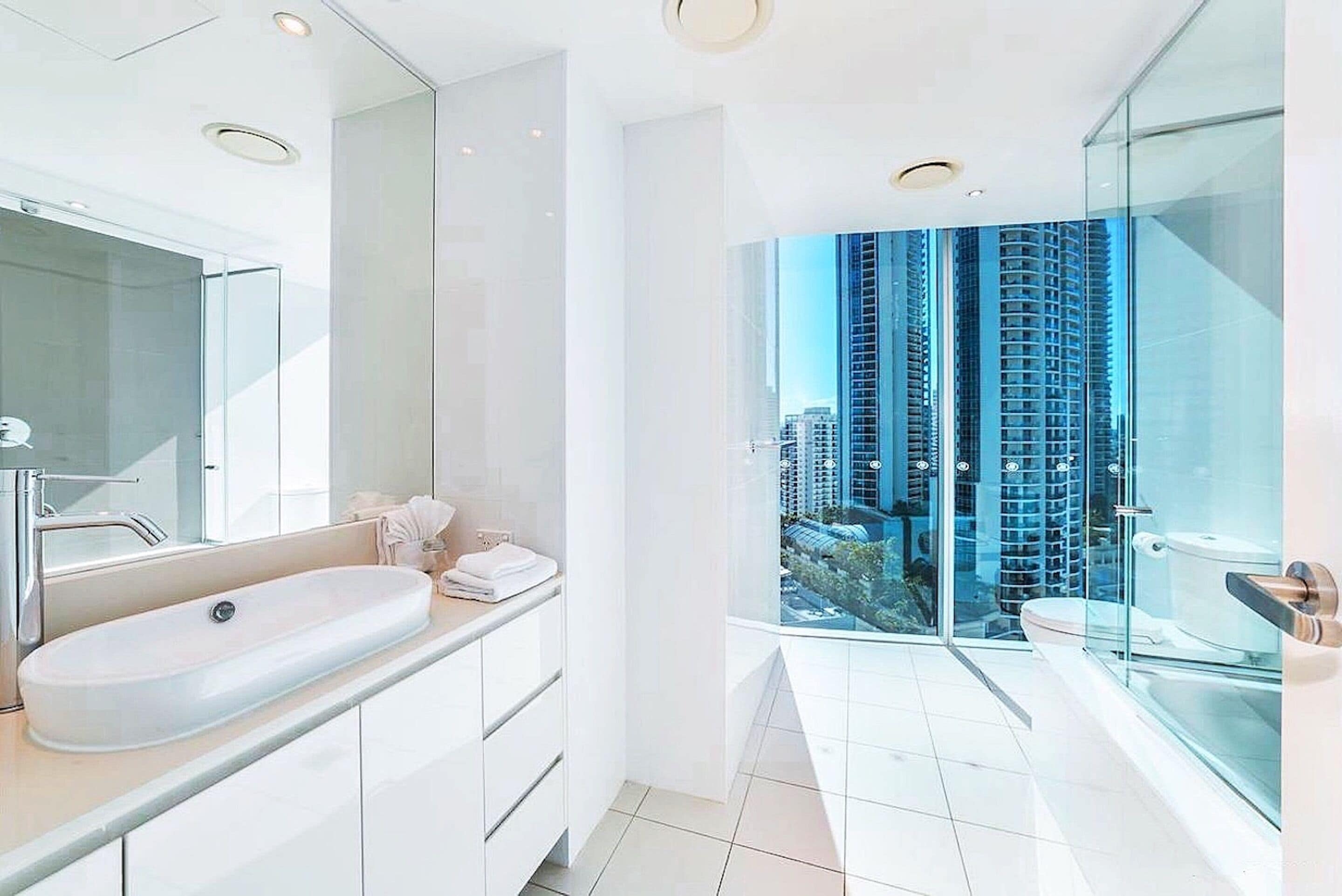 A modern bathroom with a large mirror, a white sink, and a glass-enclosed shower.