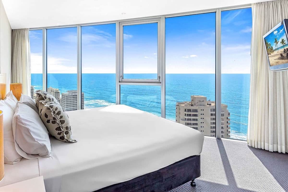 Een hotelkamer met een groot bed, uitzicht op de oceaan en een stadsgezicht op de achtergrond.