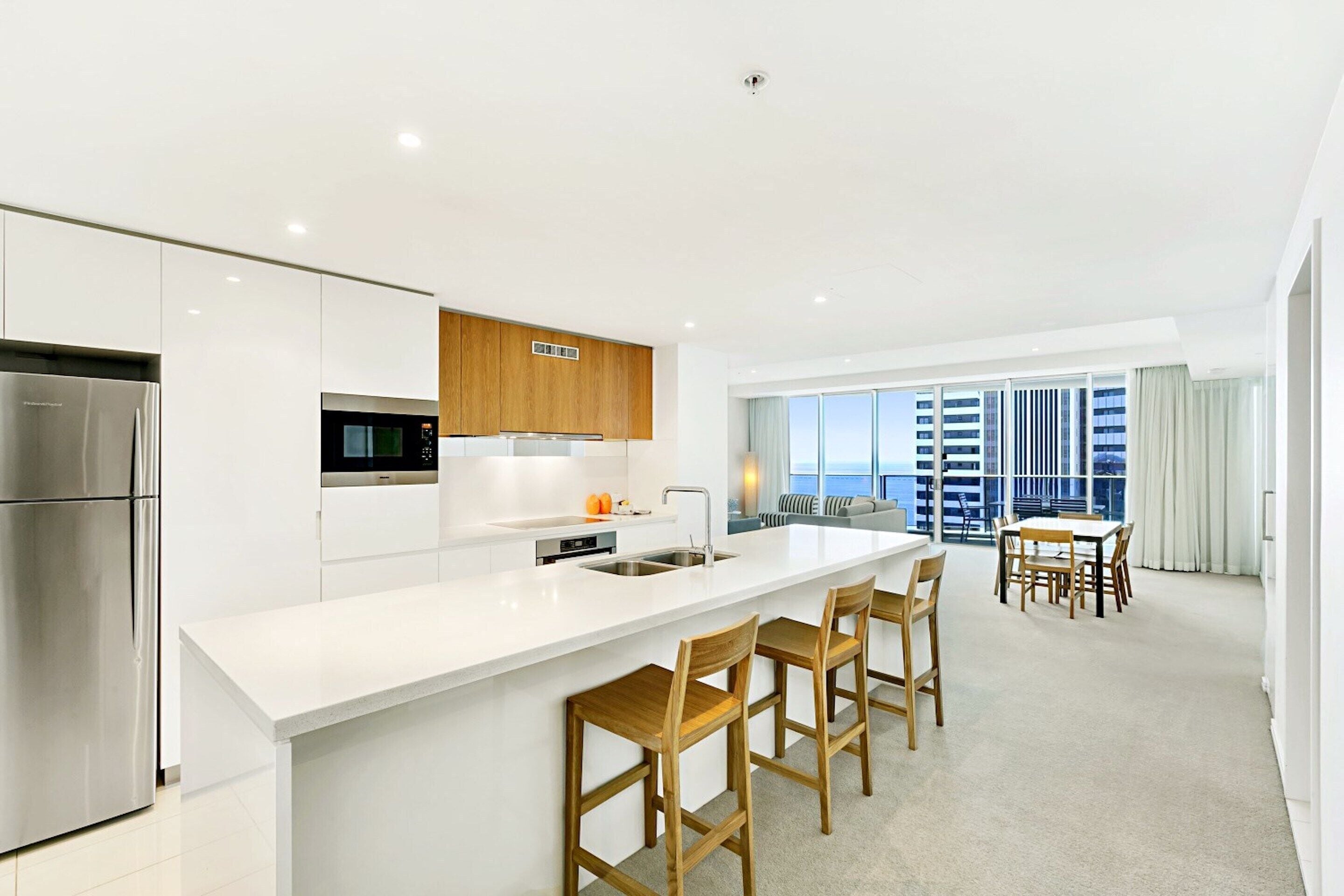 A modern kitchen with a central island, stainless steel appliances, and wooden bar stools.