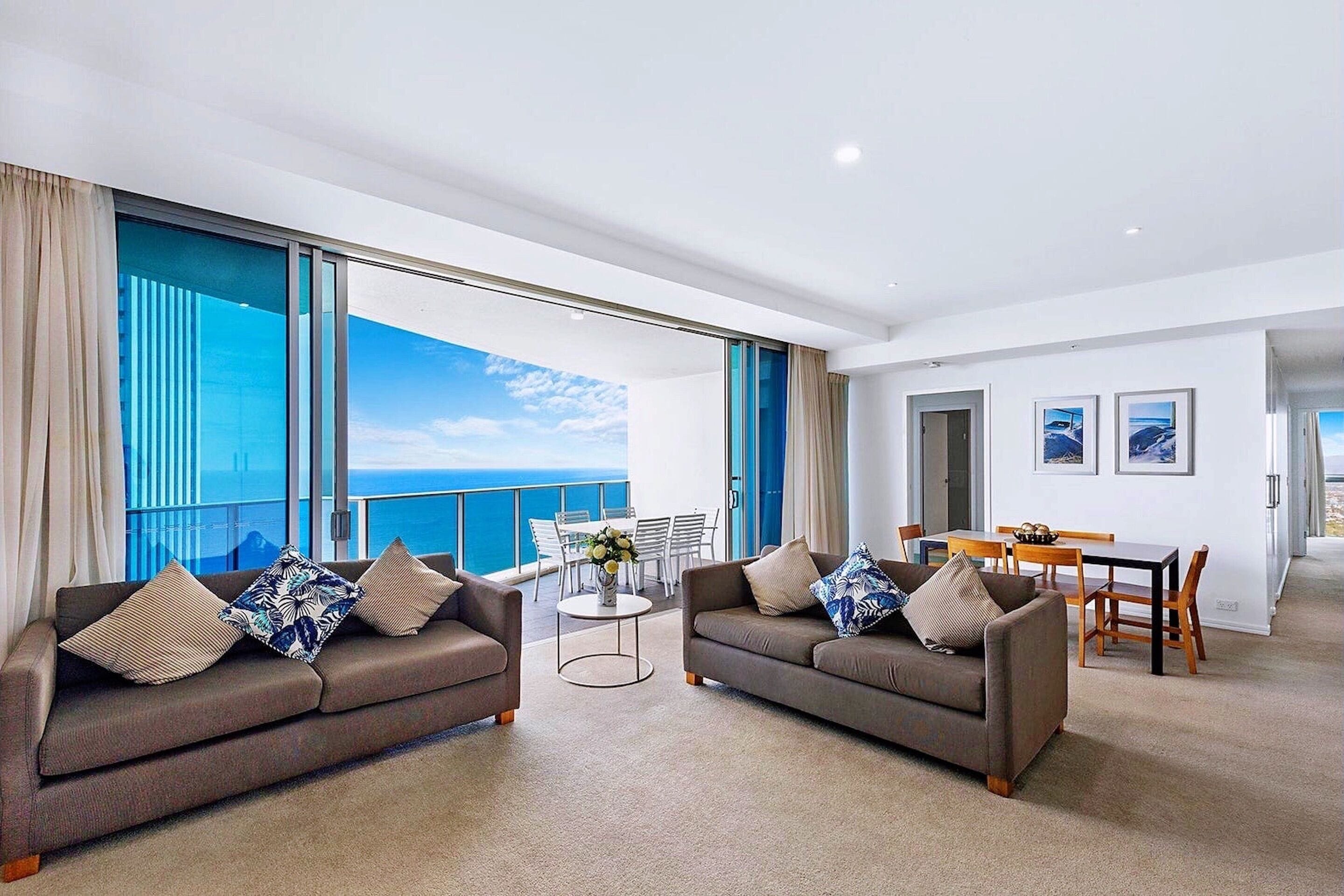 A modern living room with two sofas, a dining table, and a view of the ocean.