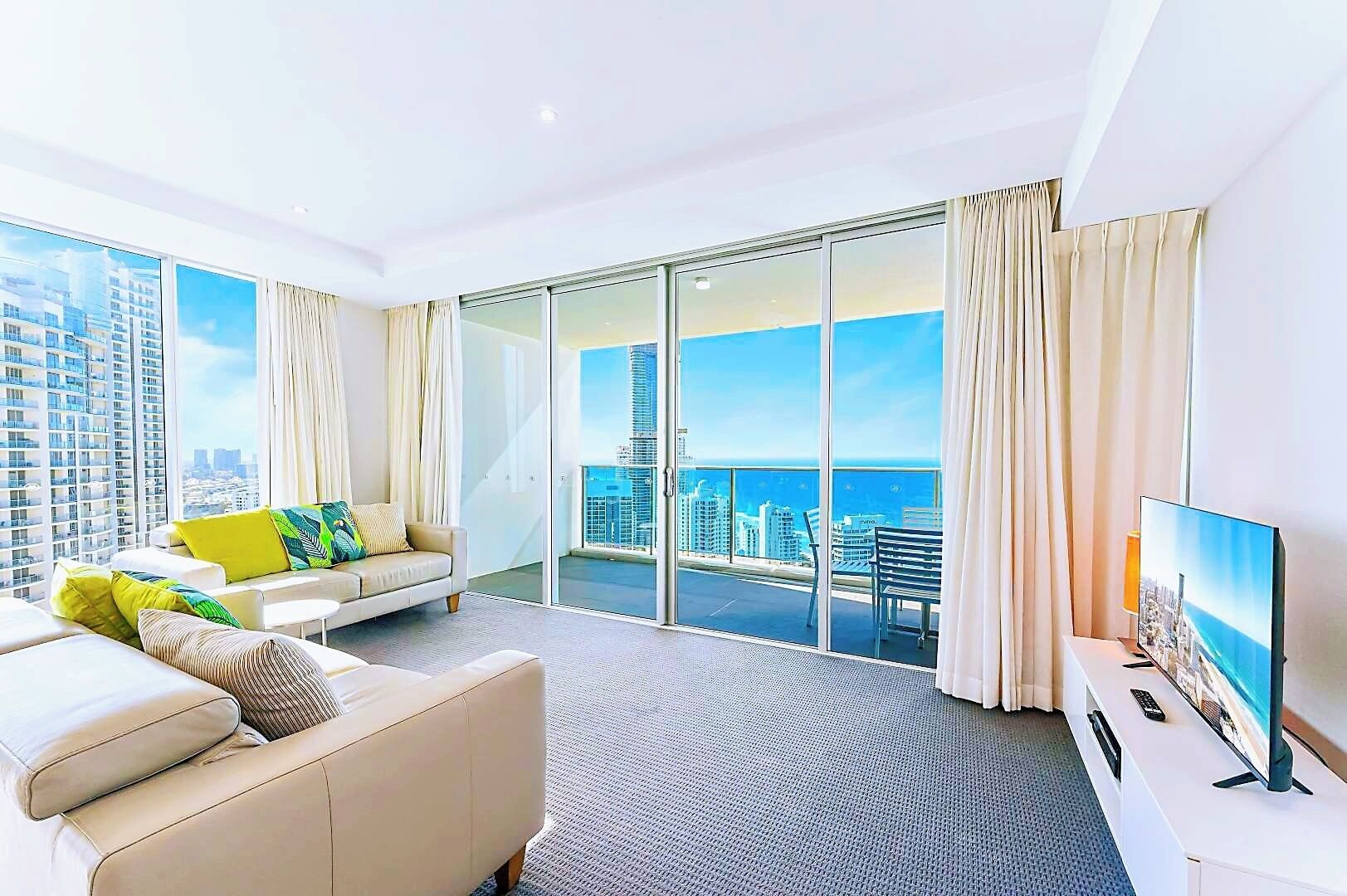 A modern hotel room with a large sliding glass door leading to a balcony with a city view.
