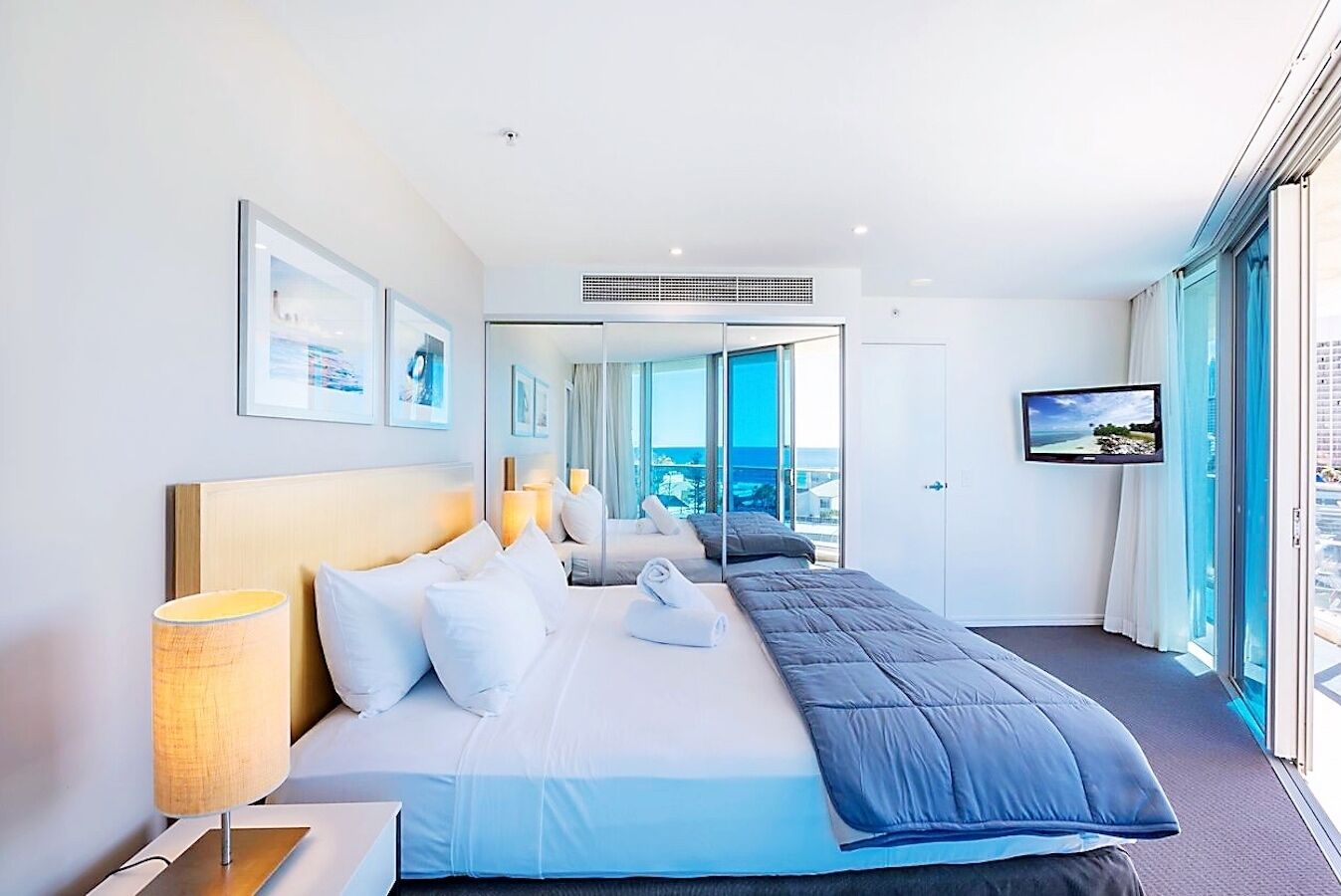 A modern hotel room with a large bed, a television, and a view of the ocean through the window.