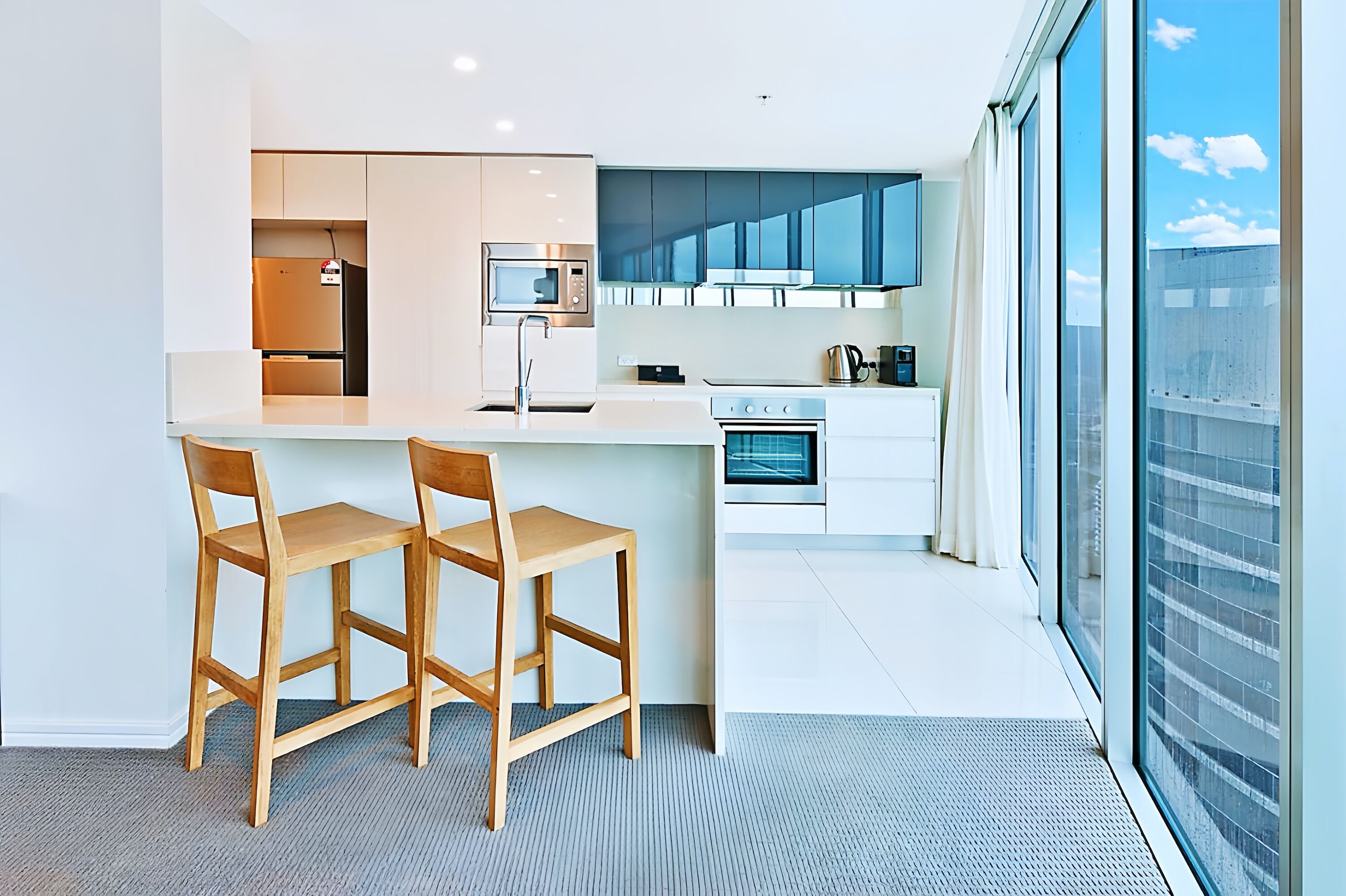 Una cocina moderna con una isla central, dos sillas de madera, un microondas, una estufa y un amplio ventanal con vistas a la ciudad.