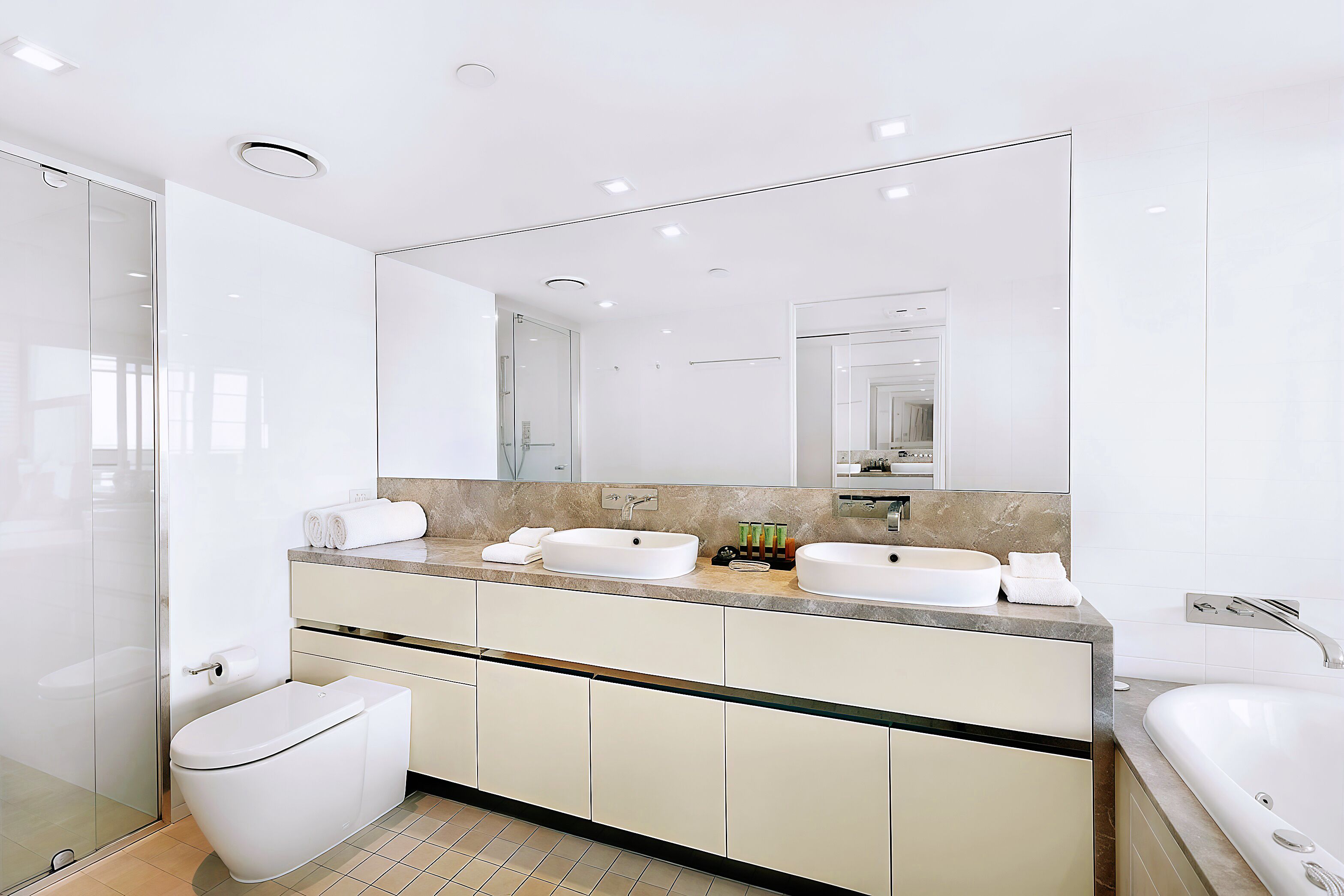 A modern bathroom with a glass shower enclosure, a toilet, a double sink vanity, and a large mirror.