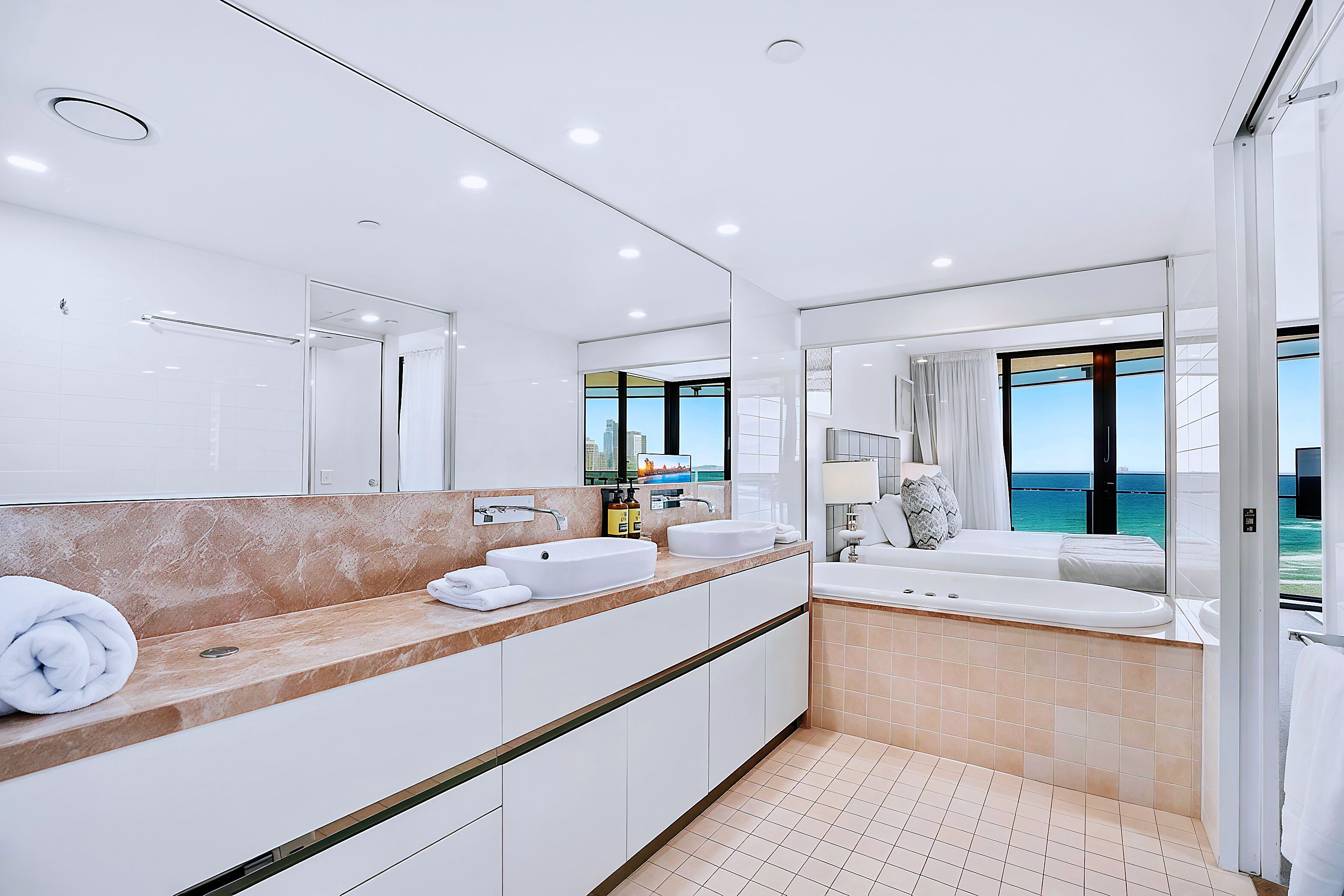 Une salle de bain moderne avec un grand miroir, deux lavabos, une baignoire et une vue sur l’océan.