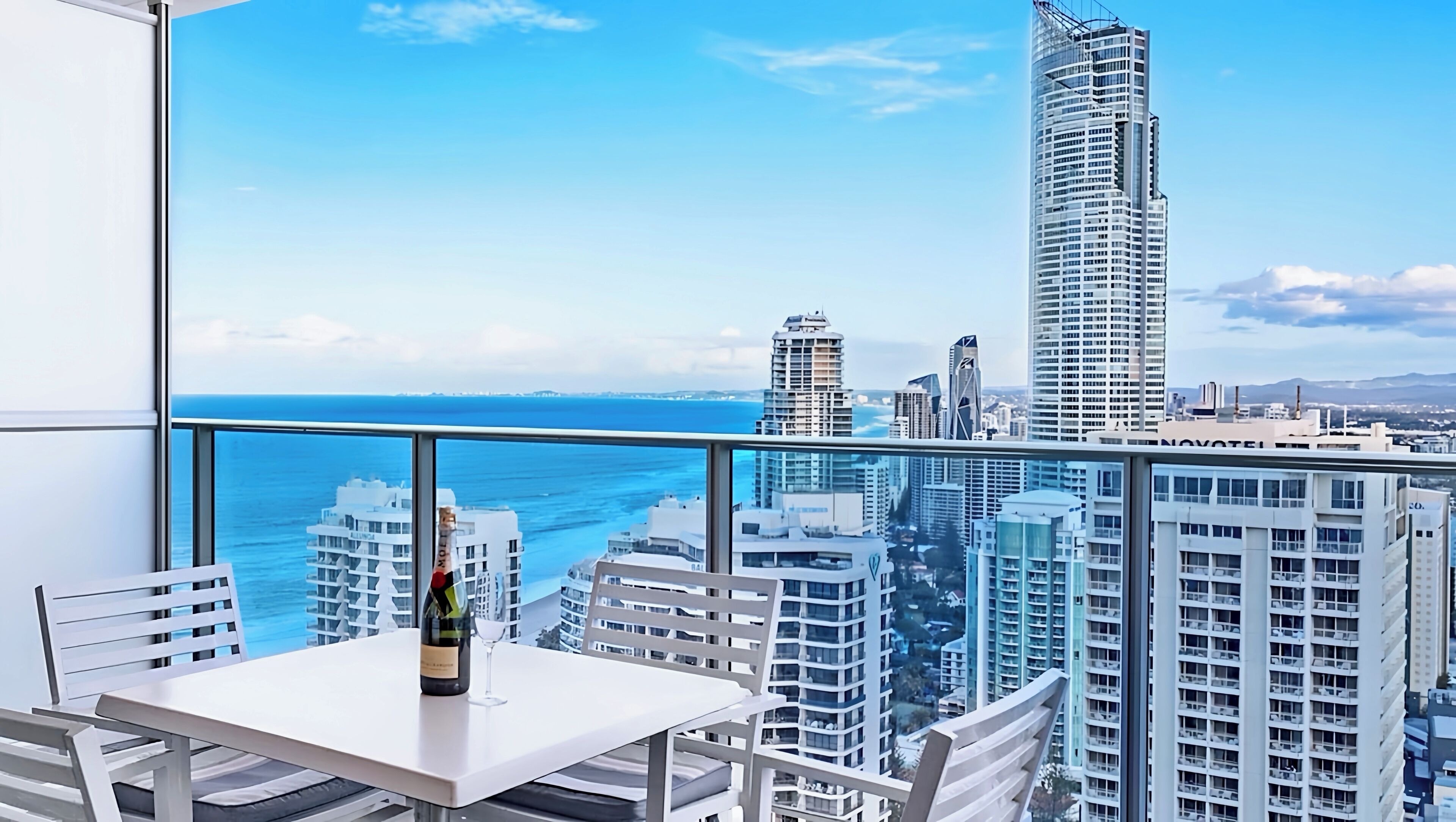 Ein Balkon mit Tisch und Stühlen, mit Blick auf eine Skyline aus hohen Gebäuden und einem klaren, blauen Himmel.
