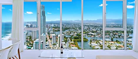Una habitación de hotel moderna con un amplio ventanal panorámico, una zona de comedor con mesa y sillas, y una botella de vino sobre la mesa.