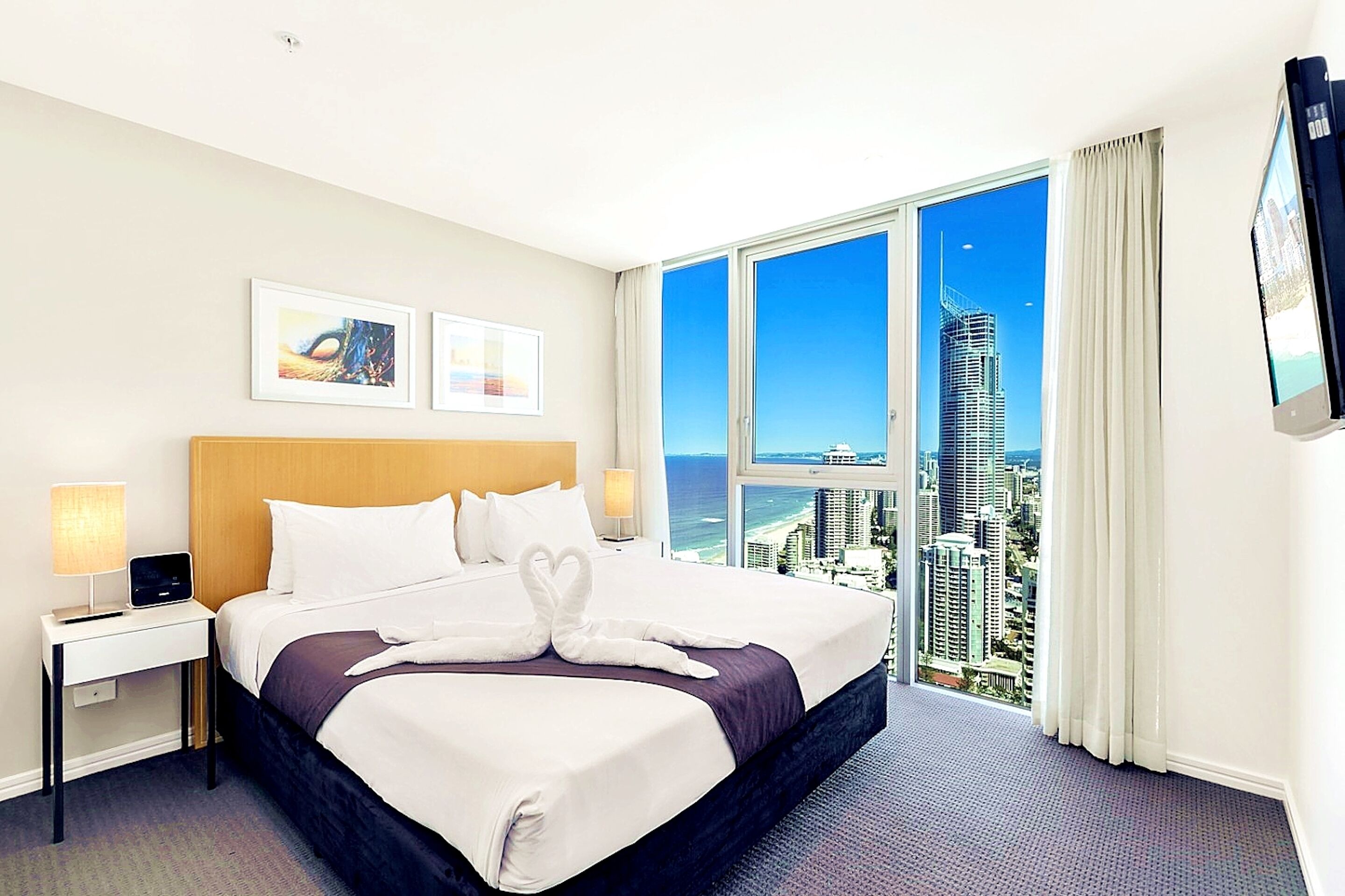 Habitación de hotel con una cama grande, dos mesitas de noche, un televisor y vistas a la ciudad.