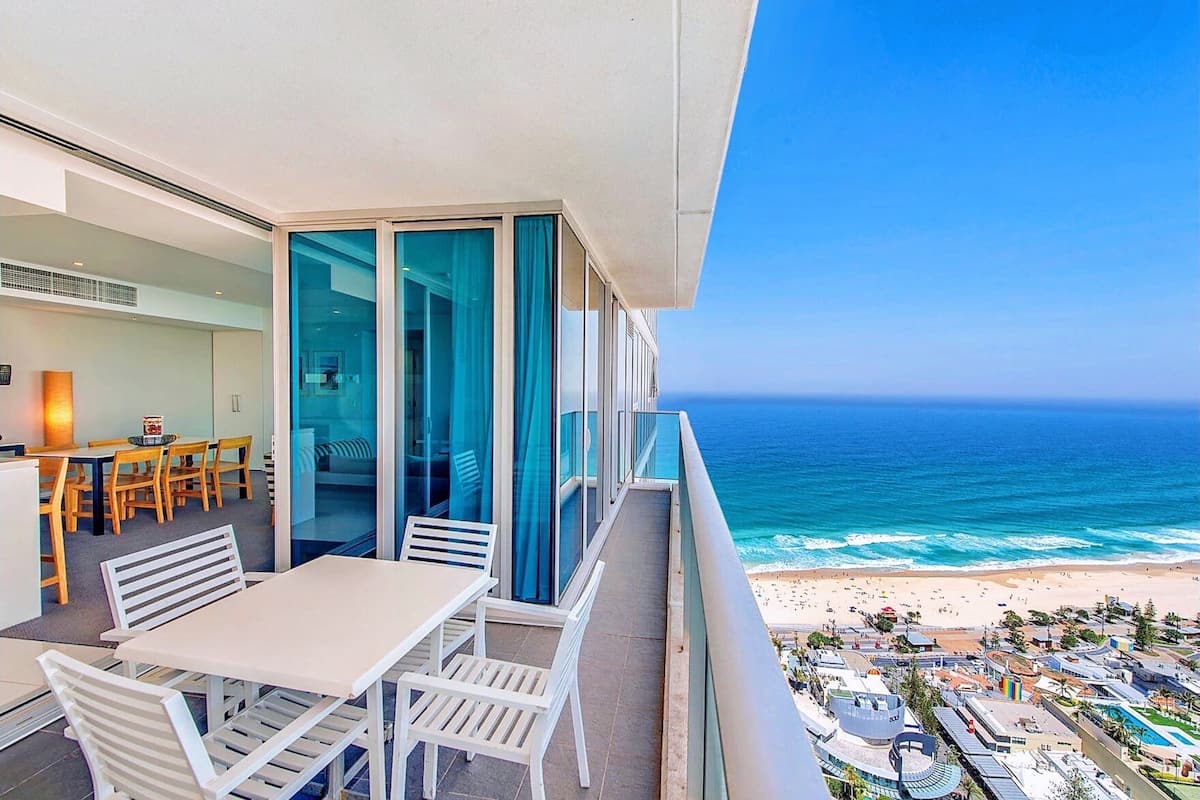 Een balkon met uitzicht op de oceaan en het strand, een eethoek met tafels en stoelen, en een modern interieur.