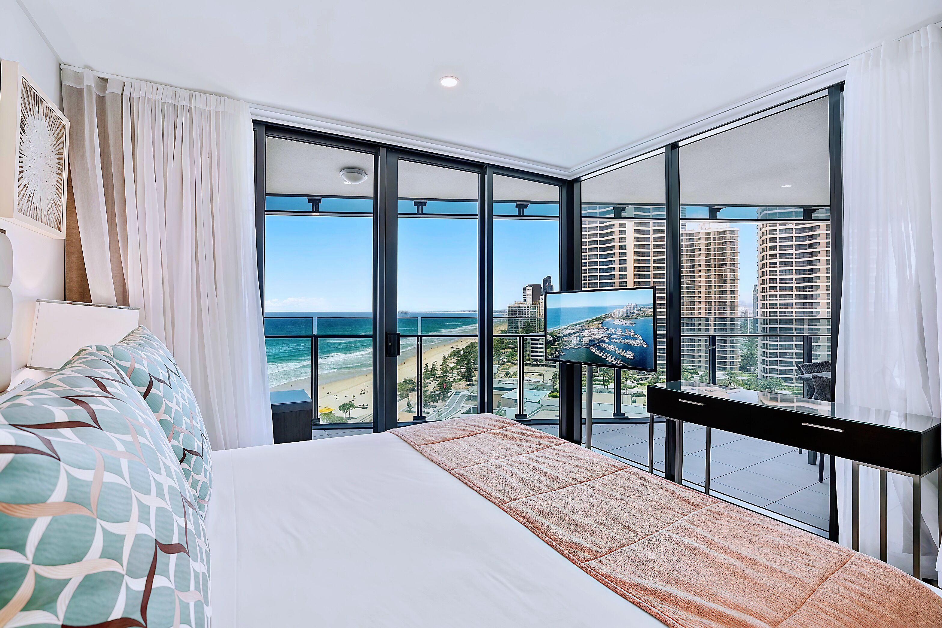 A hotel room with a large bed, a TV, and a balcony with a city view.
