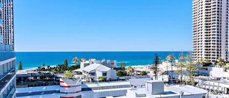A coastal urban area with modern buildings, a clear blue sky, and a view of the ocean.