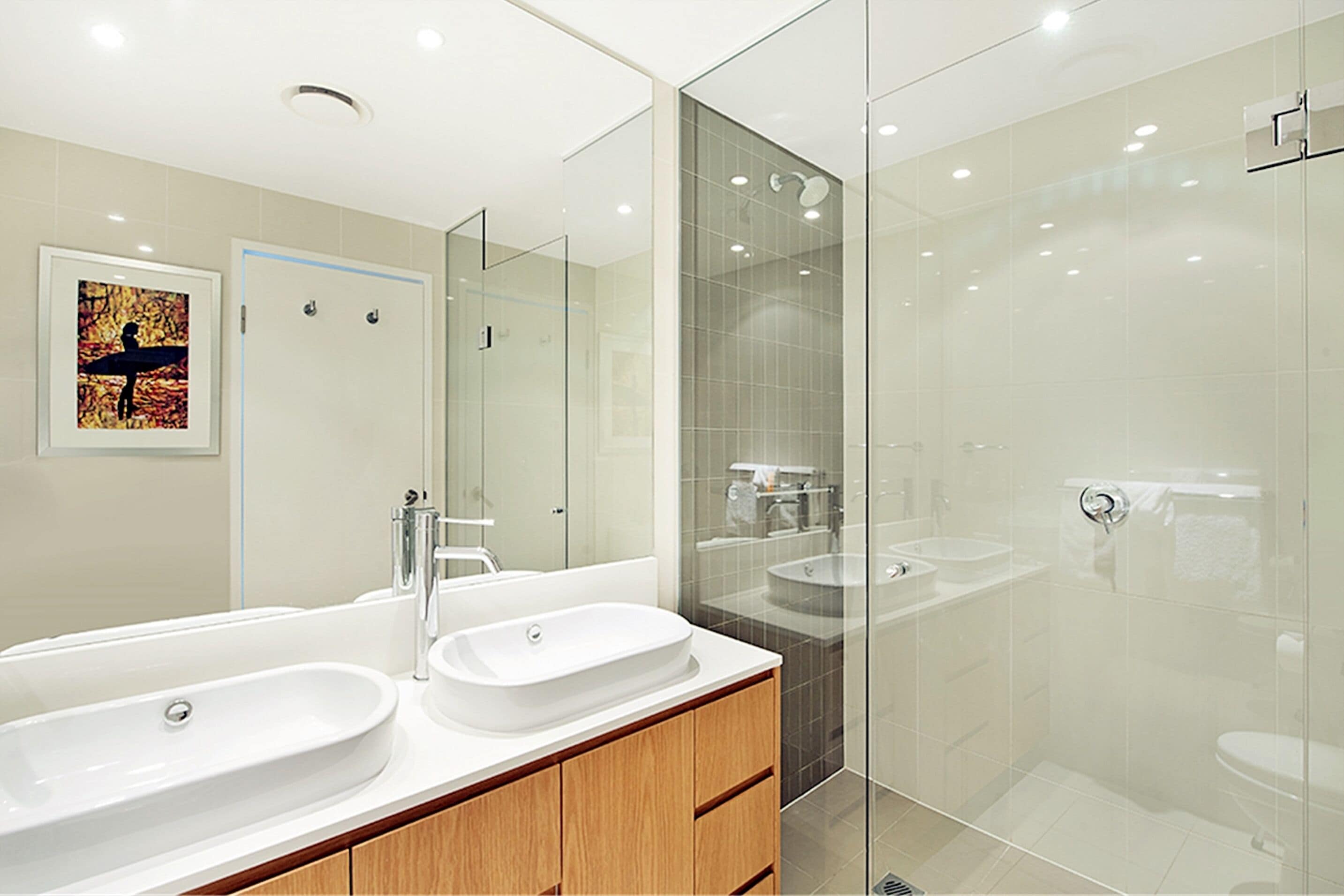 Un baño moderno con dos lavamanos, cabina de ducha de vidrio y un espejo grande.